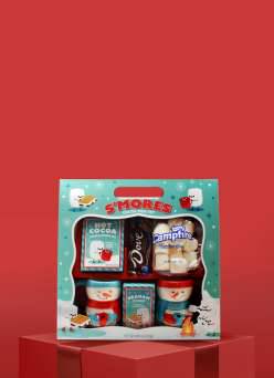 A Dove chocolate s’mores mug gift set with cocoa mix and candy on a red gift box against a red background.