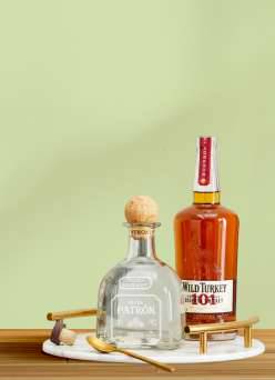 A bottle of Patrón silver tequila and a bottle of Wild Turkey 101 Kentucky Straight Bourbon on a bar cart against a light green background.